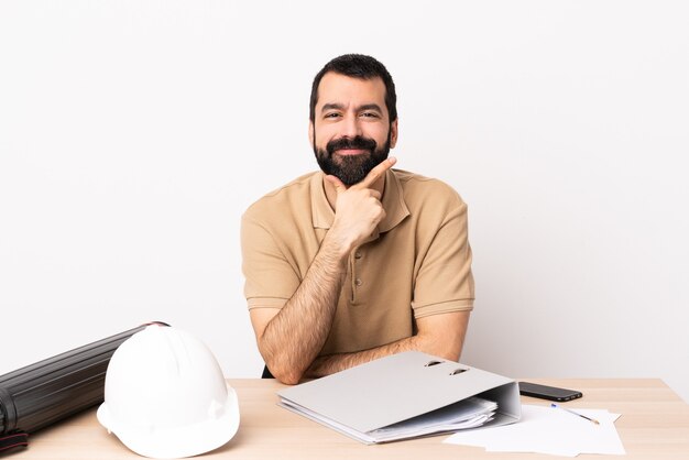 Hombre caucásico arquitecto con barba en una mesa feliz y sonriente.