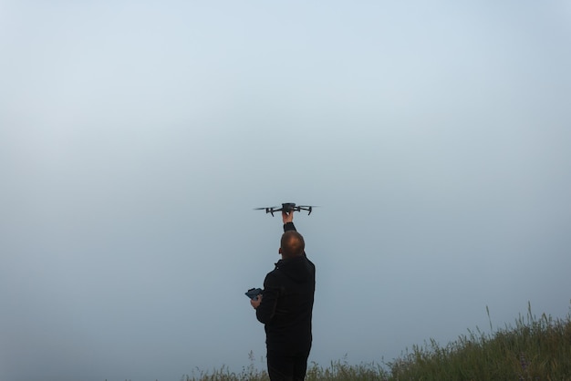 Hombre caucásico atrapando o lanzando un dron contemporáneo portátil en una mañana nublada de verano