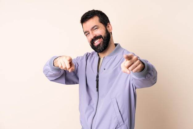 Hombre caucásico con barba con una chaqueta sobre el frente apuntando aislado con expresión feliz