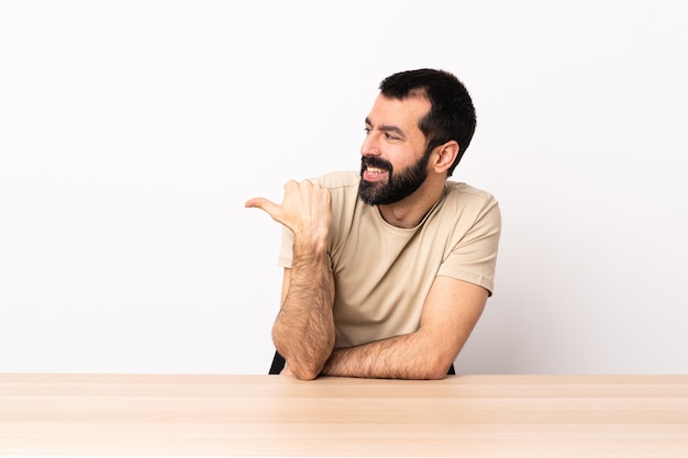 Hombre caucásico con barba en una mesa apuntando hacia el lado para presentar un producto