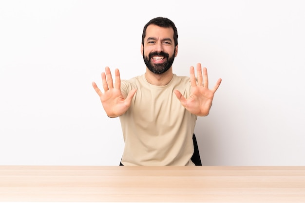 Hombre caucásico con barba en una mesa contando diez con los dedos.