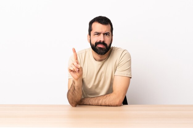 Hombre caucásico con barba en una mesa contando uno con expresión seria.