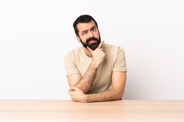 Hombre caucásico con barba en una mesa con dudas.