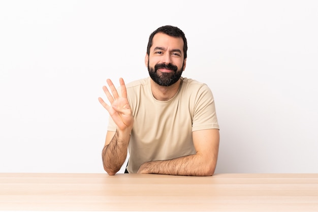 Hombre caucásico con barba en una mesa feliz y contando cuatro con los dedos