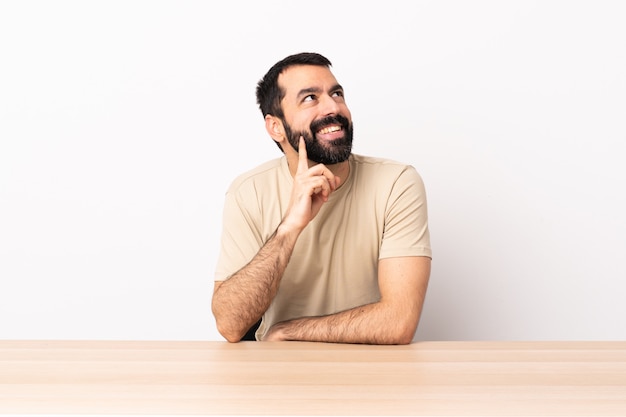 Hombre caucásico con barba en una mesa pensando una idea mientras mira hacia arriba