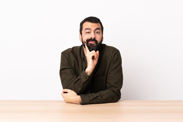 Hombre caucásico con barba en una mesa y pensando.