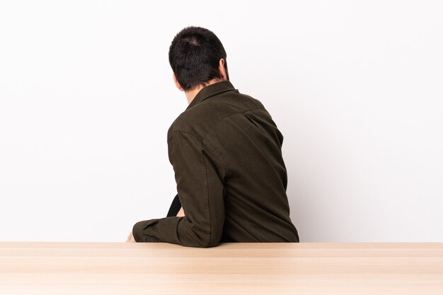 Hombre caucásico con barba en una mesa en posición trasera y mirando de lado.