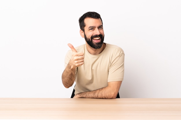 Hombre caucásico con barba en una mesa con el pulgar hacia arriba porque ha sucedido algo bueno.