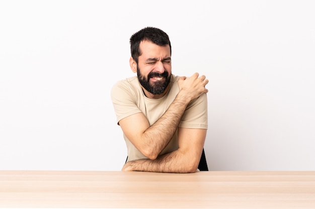 Foto hombre caucásico con barba en una mesa que sufre de dolor en el hombro por haber hecho un esfuerzo