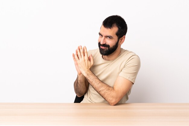 Hombre caucásico con barba en una mesa tramando algo.