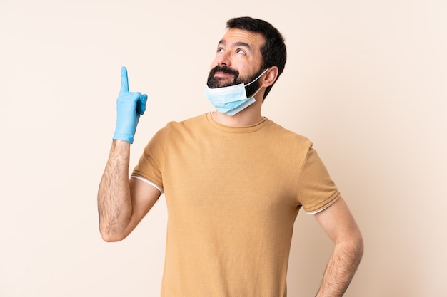 Hombre caucásico con barba protegiendo con una máscara y guantes sobre la pared apuntando una gran idea