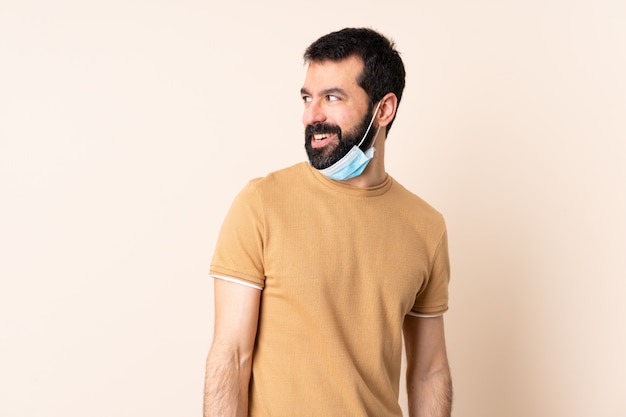 Hombre caucásico con barba protegiendo con una máscara y guantes sobre pared