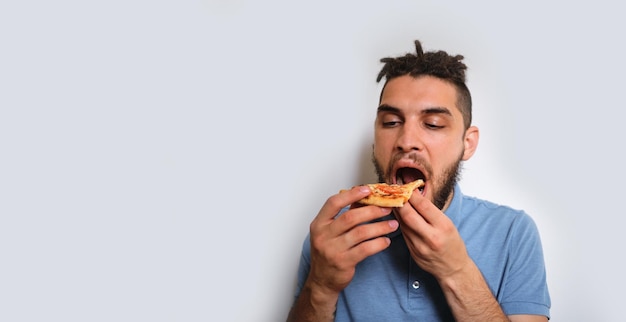 Hombre caucásico con barba y rastas come pizza sobre fondo blanco neutro Banner horizontal