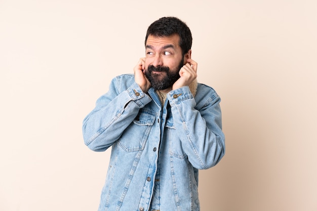 Hombre caucásico con barba sobre pared aislada frustrado y cubriendo las orejas