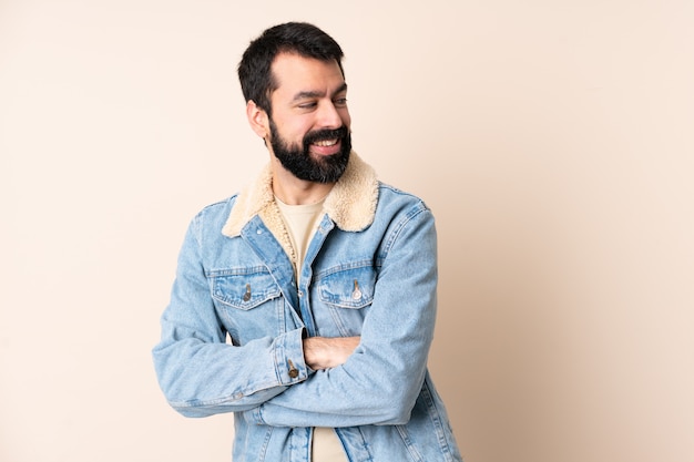 Hombre caucásico con barba sobre la pared con los brazos cruzados y feliz