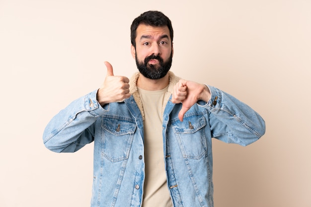 Hombre caucásico con barba sobre la pared haciendo buena-mala señal