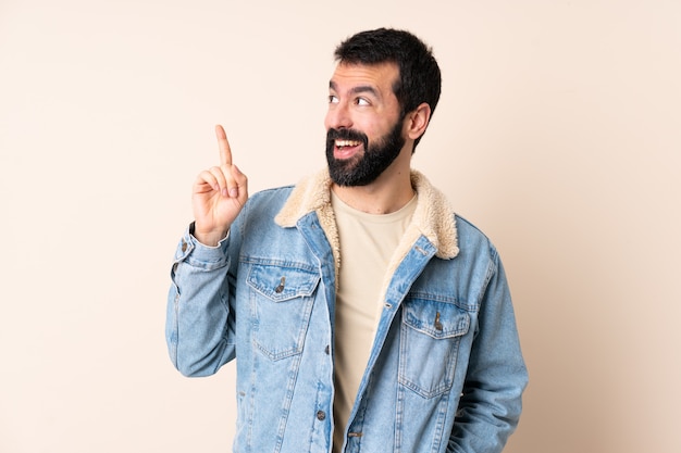 Hombre caucásico con barba sobre la pared con la intención de darse cuenta de la solución mientras levanta un dedo