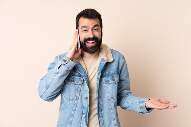 Hombre caucásico con barba sobre la pared manteniendo una conversación con el teléfono móvil con alguien