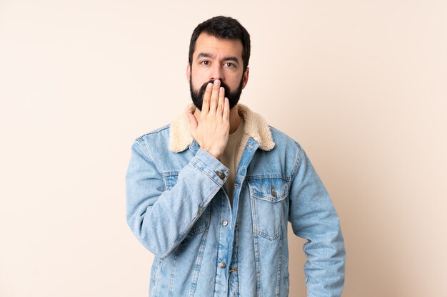 Hombre caucásico con barba sobre la pared que cubre la boca con la mano