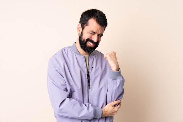 Hombre caucásico con barba vistiendo una chaqueta sobre aislado con dolor en el codo