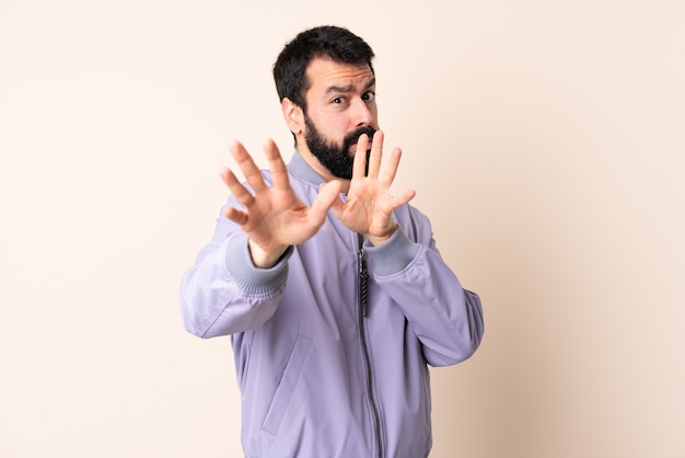 Hombre caucásico con barba vistiendo una chaqueta sobre la pared nerviosa estirando las manos al frente