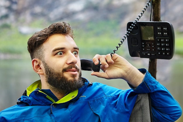 Hombre caucásico barbudo está hablando por teléfono con botón de un modelo obsoleto, con tubo de alambre trenzado.