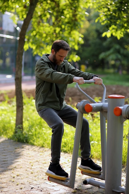 Hombre caucásico barbudo usando equipo de ejercicio público en el parque