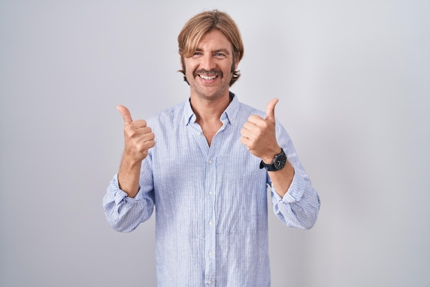 Hombre caucásico con bigote sobre fondo blanco signo de éxito haciendo gesto positivo con la mano, pulgares arriba sonriendo y feliz. expresión alegre y gesto ganador.