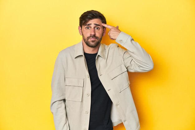 Hombre caucásico en camisa gris estudio disparado en amarillo mostrando un gesto de decepción con el dedo índice