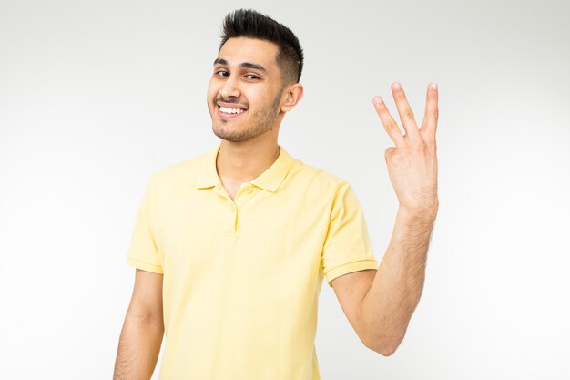 Hombre caucásico en una camiseta amarilla muestra tres dedos en un blanco aislado