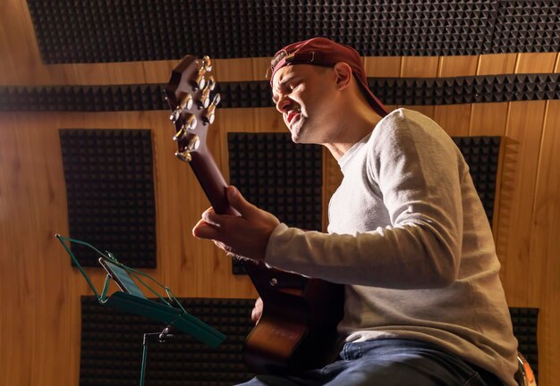 Foto hombre caucásico canta una canción tocando la guitarra sosteniendo un instrumento musical en las manos sentado en una silla en