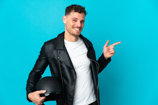 Hombre caucásico con un casco de motocicleta aislado en la pared azul que señala el dedo hacia el lado