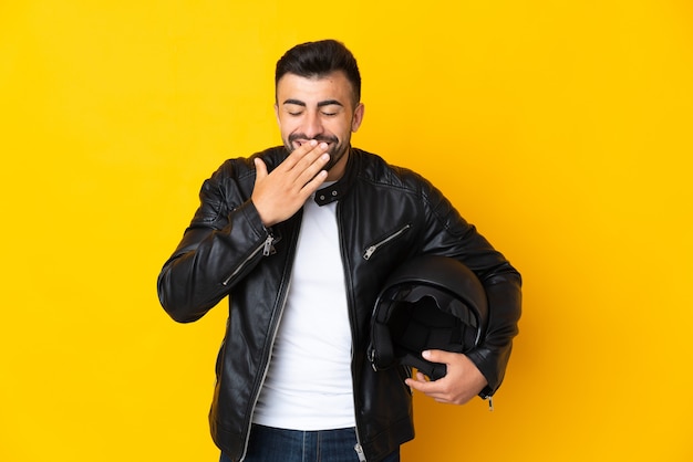 Hombre caucásico con un casco de motocicleta sobre pared amarilla aislada feliz y sonriente cubriendo la boca con la mano