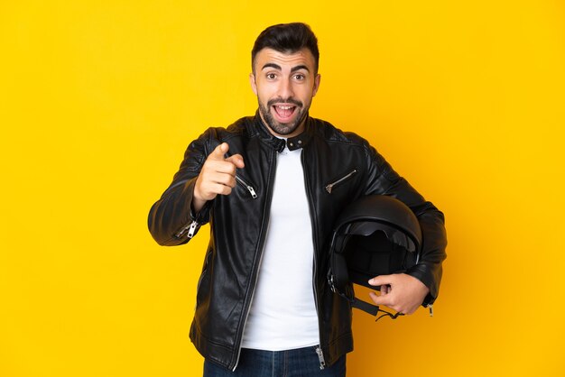 Foto hombre caucásico con un casco de motocicleta sobre pared amarilla aislada sorprendido y apuntando hacia el frente