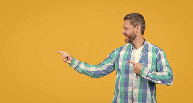 hombre caucásico casual señala con el dedo en el estudio foto de un hombre caucásio que usa una camisa a cuadros hombre caucàsico que usa un estilo casual hombre caucázico barbudo con una camisa casual aislado sobre un fondo amarillo