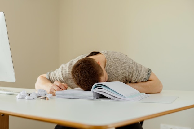 Hombre caucásico deprimido con dolor de cabeza sentado en su escritorio en la oficina El joven empleado estresado tiene problemas en el trabajo El hombre de negocios tiene agotamiento Salud mental Abrumado por el trabajo Estrés de fecha límite