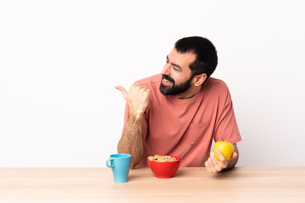 Hombre caucásico desayunando en una mesa apuntando hacia el lado para presentar un producto.