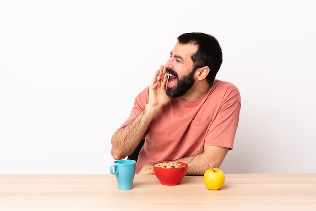 Hombre caucásico desayunando en una mesa gritando con la boca abierta a un lado