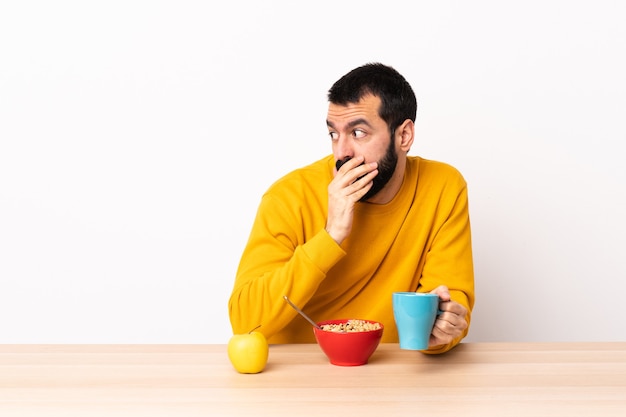 Hombre caucásico desayunando en una mesa haciendo gesto de sorpresa mientras mira hacia un lado.