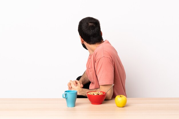 Hombre caucásico desayunando en una mesa en posición trasera.