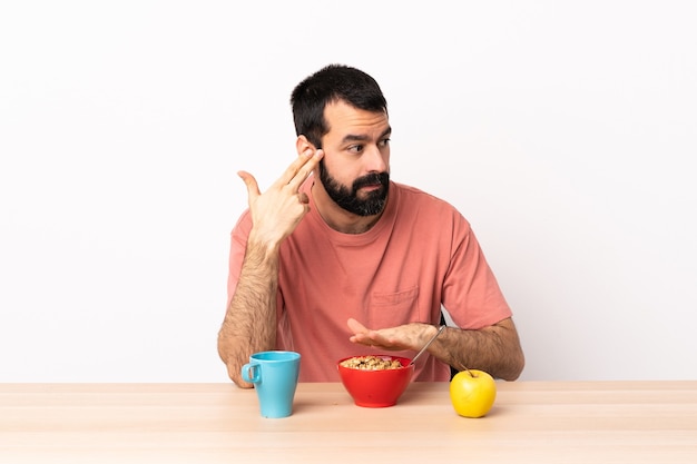 Hombre caucásico desayunando en una mesa con problemas para hacer gestos de suicidio.