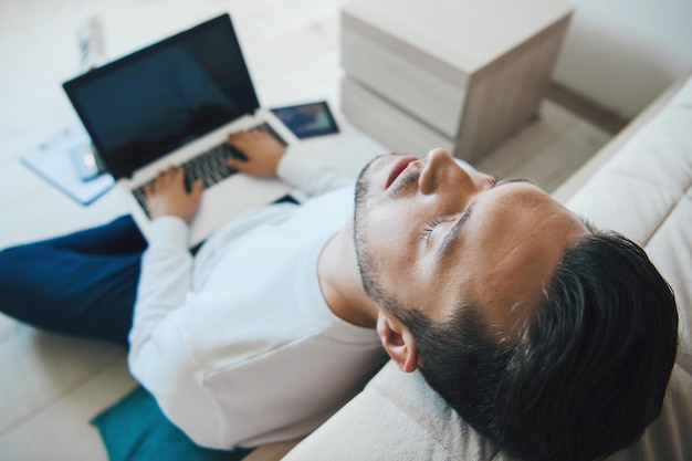 Hombre caucásico durmiendo y acostado en el piso inclinando la cabeza desde el sofá después de trabajar duro y video c ...