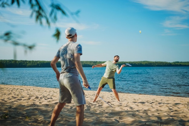 Hombre caucásico e hijo adolescente jugando al bádminton en la orilla del lago Concepto de padres y adolescentes