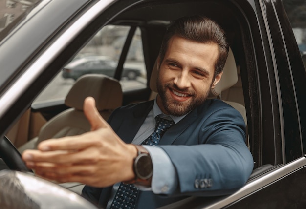 Hombre caucásico elegante feliz en traje sentado al volante de un coche moderno