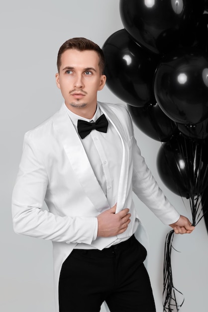 Foto hombre caucásico elegante con traje blanco y esmoquin con globos de aire negro sobre fondo blanco
