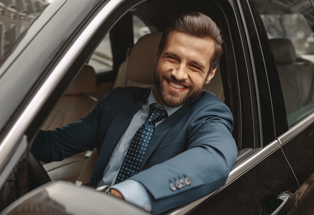 Hombre caucásico elegante en traje sentado al volante del coche