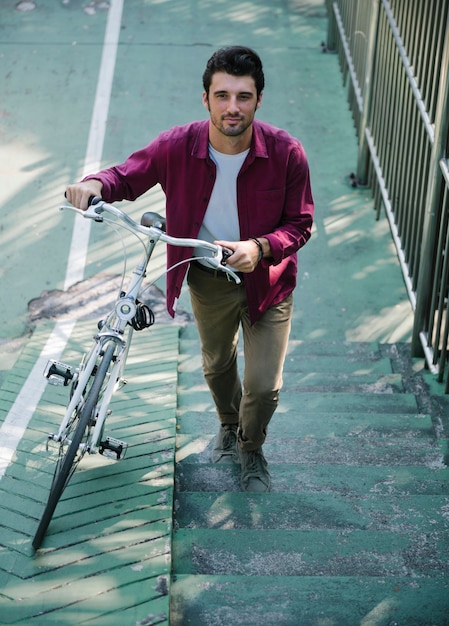 Hombre caucásico empujando su bicicleta cuesta arriba