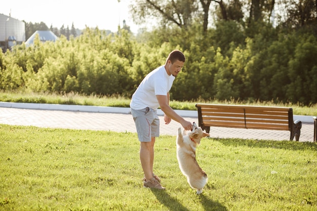 Hombre caucásico está entrenando a su perro Corgi, alimentándolo. Al aire libre en el parque en verano.