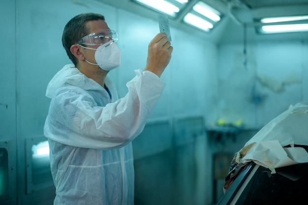 El hombre caucásico está revisando la pintura de color en el taller de pintura mecánica de reparación