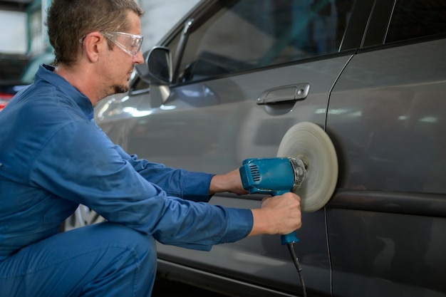 El hombre caucásico está usando una máquina pulidora de automóviles en un taller de pintura mecánica de reparación